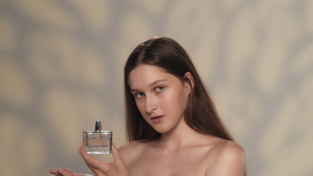 Brunette female model with long hair and natural makeup holding a perfume