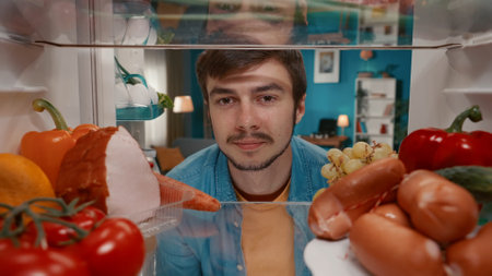 Portrait of a smiling man at the open refrigerator. A man is satisfied with the abundance of food in...