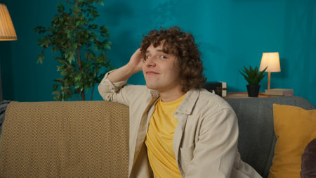 Young man in casual clothing, sitting on the sofa in the living room thinking about something good...