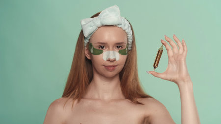 A woman with patches under the eyes and with a plaster from blackheads, with a hairband on her head on a green screen. A woman demonstrates an ampoule of hair serum.の写真素材