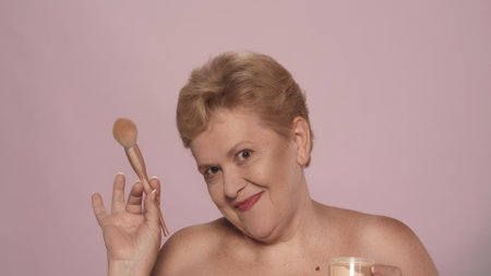 Elegant blonde woman holding a brush and powder jar, looking at the cameraの写真素材