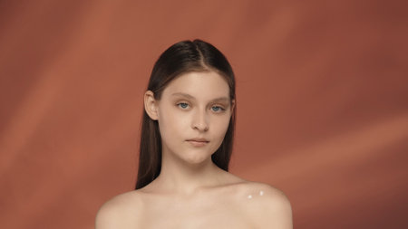 Portrait of a seminude woman with applied cream on her shoulder in the studio on a red background close up. The concept of natural beauty, cosmetology, skin care.の写真素材