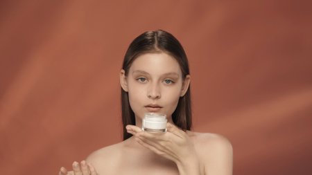 A woman holds a jar of cosmetic cream. Seminude woman with a jar of cream in the studio on a red background. The concept of beauty, cosmetology, care.の写真素材