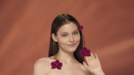 A young woman with orchid flowers in her hair, near her face and on her chest. Portrait of a seminude woman with orchid flowers in the studio on a red background.の写真素材