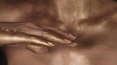 Closeup camera shot of the woman hands and body covered in dried golden paintの写真素材