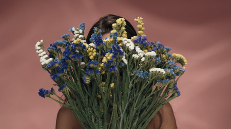 A woman hides her face behind a bouquet of wildflowers. A woman with problem skin, covers her face...