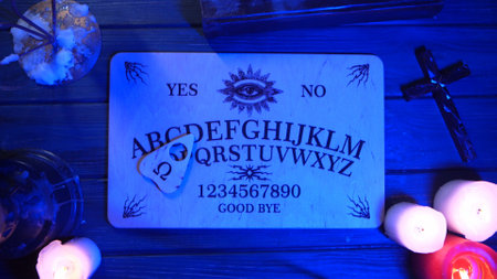 Close up shot of a wooden board with a planchette on a table surrounded by candles, candlesticks and...
