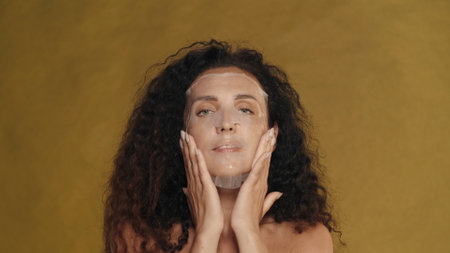 Woman in white cosmetic sheet mask on her face. Portrait of a seminude woman in the studio on a yellow background. The concept of beauty, cosmetology, care.の写真素材