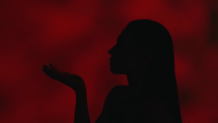 Close up side profile video of a young woman blowing a feather away from her palm on a dark red...
