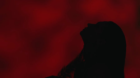 Close up side profile shot of a young woman gracefully leaning back with her head up on a dark red background.の写真素材