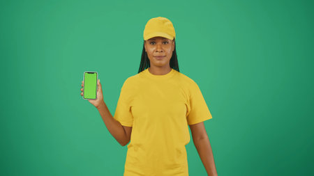 Delivery woman in yellow uniform holding smartphone. Advertising area, workspace mockup.