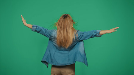 Woman tourist standing holding hands up, wind blows her hair. Isolated on green background.の写真素材