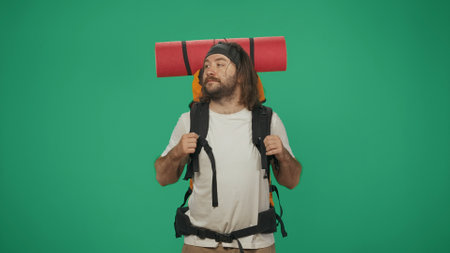 Man tourist with backpack looks around with relaxed face. Isolated on green background.の写真素材