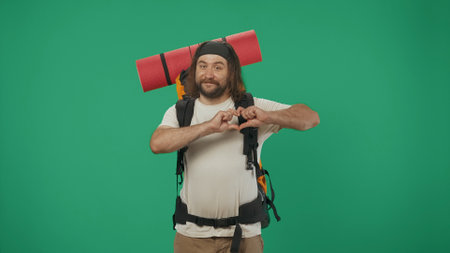 Man tourist with backpack with amazed face, shows hand heart. Isolated on green background.