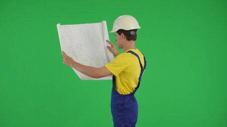 Medium green screen isolated chroma key shot of a young construction worker studying and comparing his plan to the surroundings.の写真素材