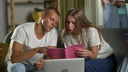 Medium shot of a boy and a girl sitting on a couch in a group of teens, young people, friends, studying, preparing for an exam, discussing, looking at their notes.の写真素材