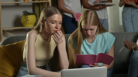 Medium shot of two girls sitting on a couch in a group of teens, young people, friends studying,...