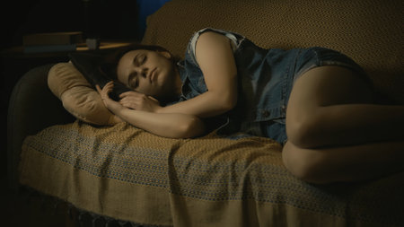 Closeup shot of young girl in casual clothes calmly laying sleepping on the sofa in the dark living room.の写真素材