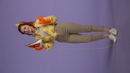 Vertical photo. Woman in casual clothing and rubber gloves holding iron, showing ok sign, smiling at...