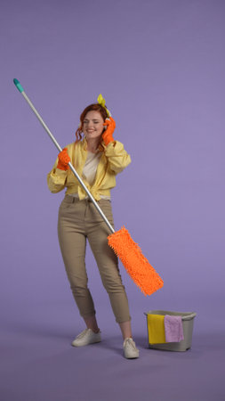 Vertical photo. Woman in casual clothing and rubber gloves in headphones listening music, dancing...
