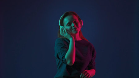 A young redhaired woman wearing white wireless headphones listens to DJ music and dances. Woman in...