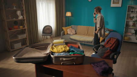 Shot of a teenager, teen, young man having a call on the background while packing a suitcase laying on the foreground, discussing something.の写真素材