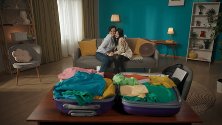 Mother sits on the couch with her daughter. They are hugging warmly, saying goodbyes. The women are looking at the suitcase laying in front of them.の写真素材