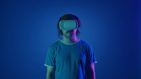 A man wearing virtual reality glasses in a studio on a blue background in pink and green neon light.の写真素材