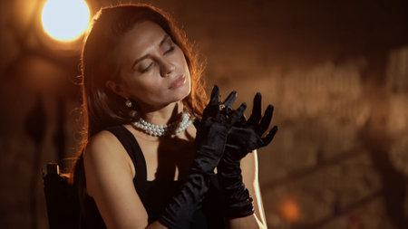 Closeup shot of brunette woman in black dress and silk gloves sitting on directors chair putting on diamond ring.の写真素材