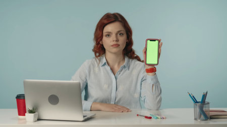 Medium isolated shot of a young woman looking at the camera and holding a phone with advertising...