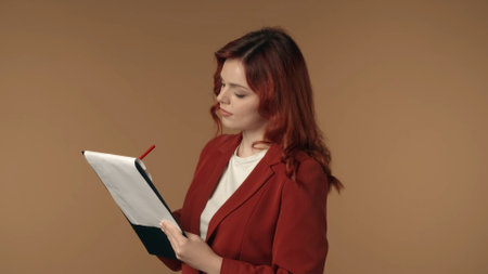 Medium isolated shot of a satisfied, happy and active young woman writing on paper in a folder, planchette, looking concentrated.の写真素材