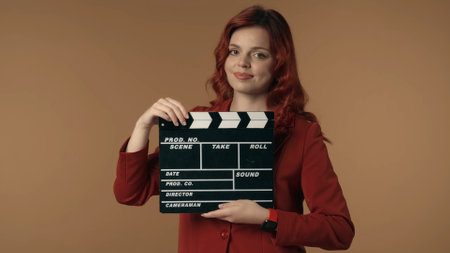 Medium isolated shot satisfied, happy and relaxed young woman holding a closed movie clicker, slate, clapperboard in front of herself.の写真素材