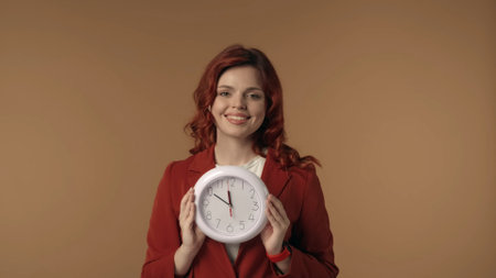 Medium isolated shot of a satisfied, happy and active young woman holding a clock in front of herself, looking at the camera and smiling.の写真素材