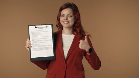 Medium isolated shot of a satisfied, happy and active young woman holding a contract, an agreement in her hands, smiling at the camera and giving a thumbs up.の写真素材