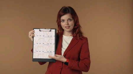 Medium isolated shot of a satisfied, happy and active young woman holding a folder, planchette in her hands and explaining the graphs, tables, charts it shows.の写真素材
