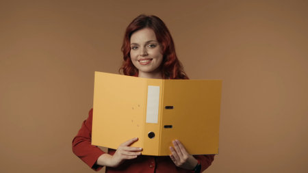 Medium isolated shot of a satisfied, happy and active young woman holding a ring binder in her hands and looking at the camera, smiling.の写真素材