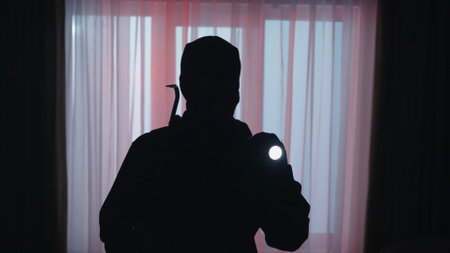 The dark silhouette of a thief in the evening in an apartment illuminated by red light from police...