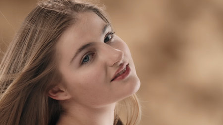 A close-up of a young blonde-haired woman against a stained background. With her head slightly turned and tilted, she looks at the camera and smiles. The wind is blowing on her, developing her hairの写真素材