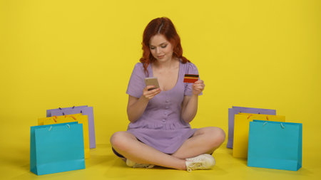 A woman makes a purchase in an online store using a smartphone and a credit card. Redhaired woman...