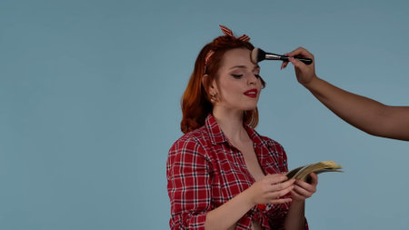 In the frame on a blue background, a red-haired young woman is getting her makeup fixed. At this...