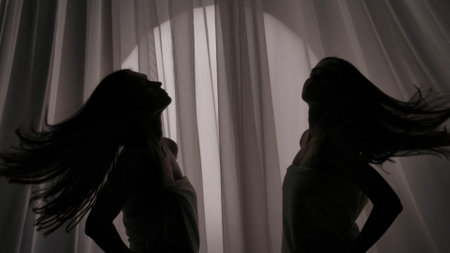 Medium side view shot of two sisters, friends, young womens silhouettes wrapped in a towel. They are swishing their hair on a curtain background in a muffled light.の写真素材