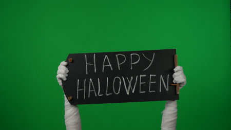 Detail green screen isolated chroma key photo capturing mummys hands holding a black chalkboard with happy halloween written on it.の写真素材