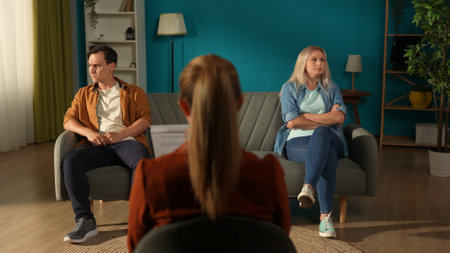 Married couple sitting on different sides of the couch in front of the female therapist. A man and a woman in a quarrel avoid eye contact. Crisis in relationships.の写真素材
