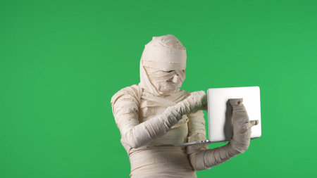 Green screen isolated chroma key photo capturing a mummy holding a laptop in its hand, typing,...