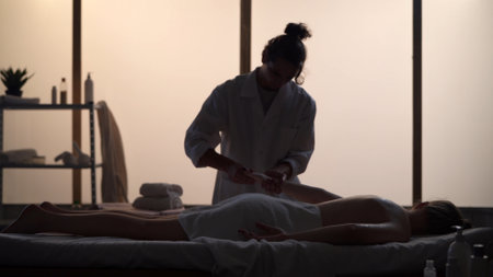 Masseur, massage specialist giving back and arm massage to his patient. Silhouettes of a woman and a man in the massaging room, spa procedure.の写真素材