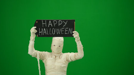 Green screen isolated chroma key photo capturing a creepy mummy holding a black chalkboard with happy halloween written on it. Medium size.の写真素材