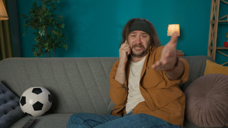 Frame shows a middle aged man sitting on a couch in an apartment. He is talking to someone on the...