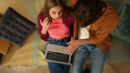 Top view capturing a young couple sitting on the couch, hugging and talking, looking at the laptop screen as if they are searching for something online.の写真素材