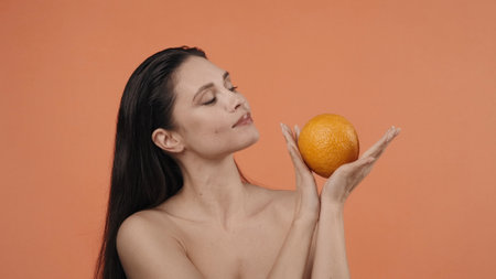 Skincare creative concept. Appealing woman holding big ripe orange fruit looking away from the camera.の写真素材