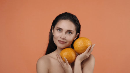 Skincare creative concept. Appealing woman posing with two big ripe orange fruit and looking at the camera.の写真素材